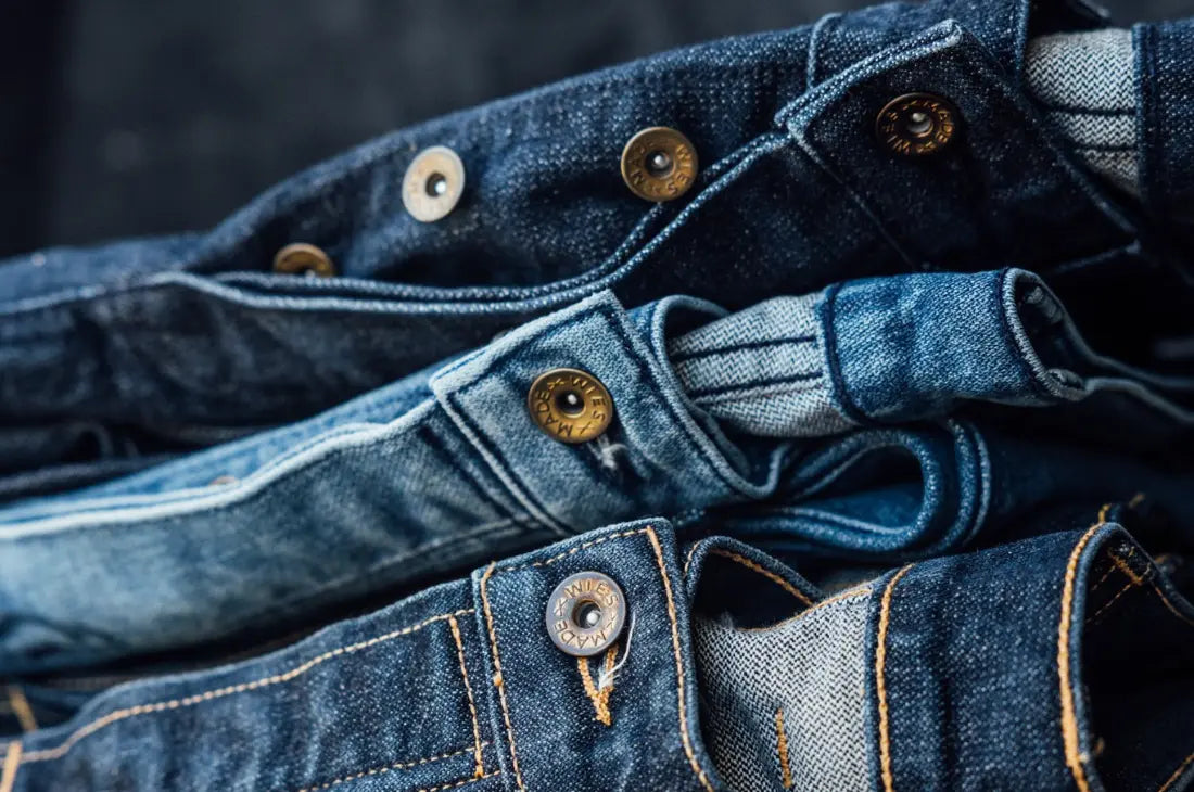 Premium denim finishes shown in a close-up of jean waistbands with detailed stitching and branded rivets.
