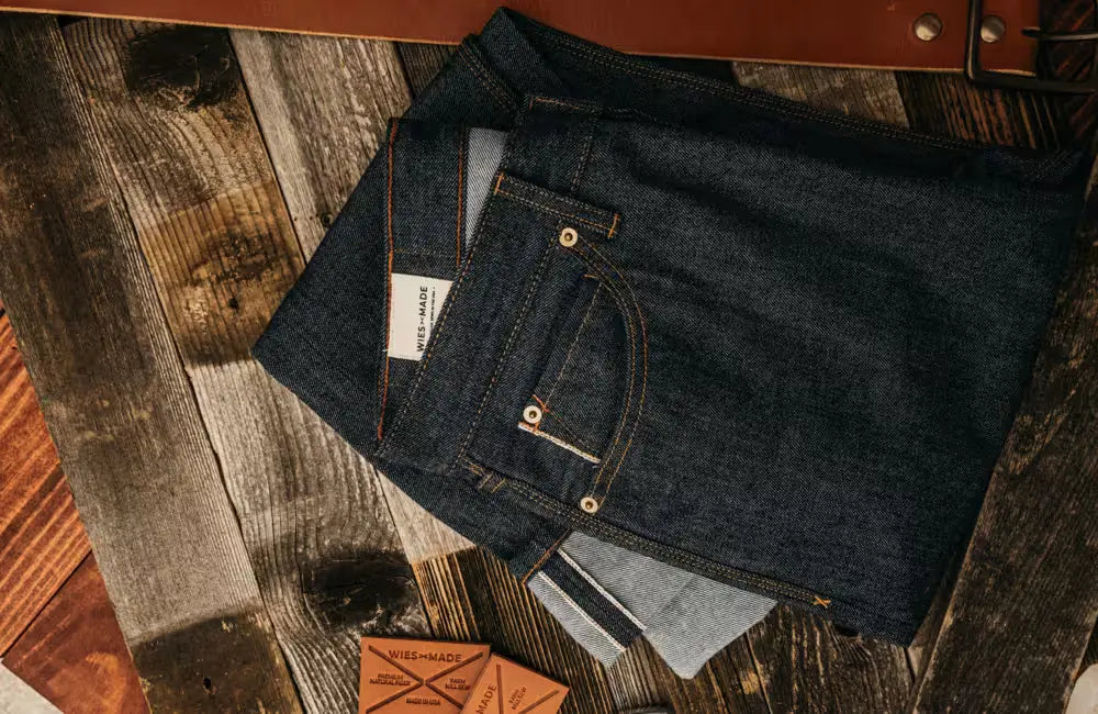 Jack Fit jeans in Raw Selvedge Denim color, neatly folded to showcase the selvedge edge and detailed stitching, placed on a rustic wooden surface with weathered planks