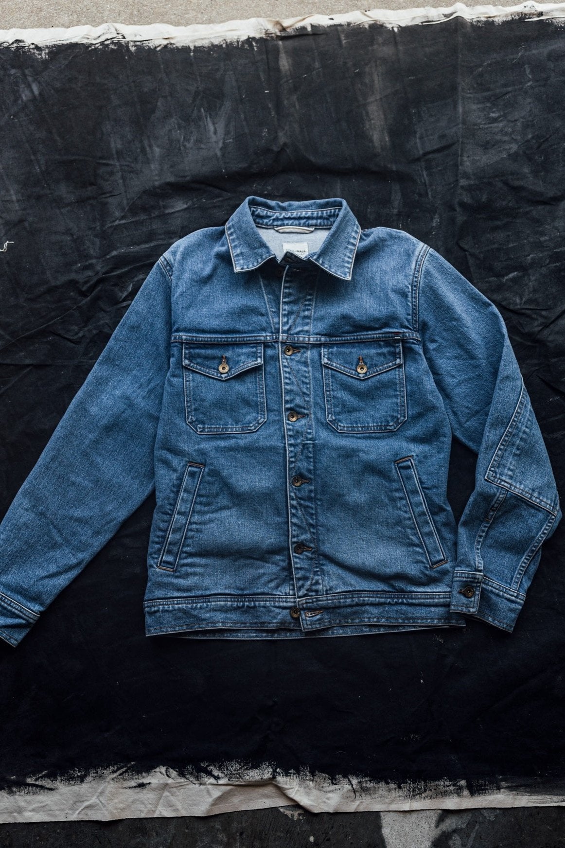 USA made denim jacket laid flat on a textured black and white fabric backdrop.