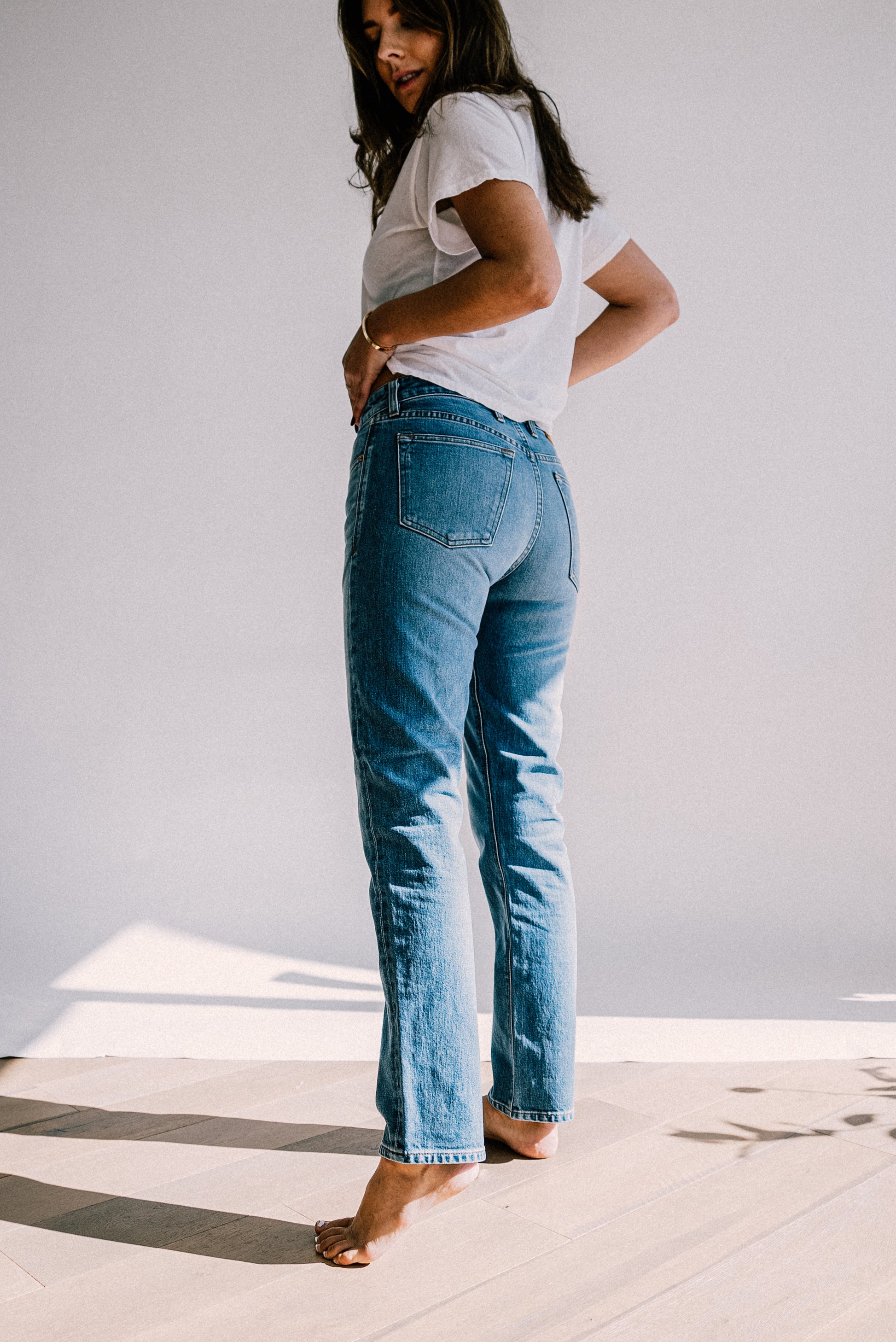 Blue jeans for women paired with a white t-shirt, shown in natural light on a wooden floor.