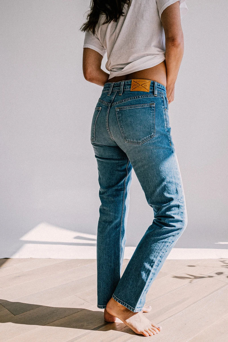Tailored fit women's denim jeans with a tan leather patch, styled with a white t-shirt and bare feet.
