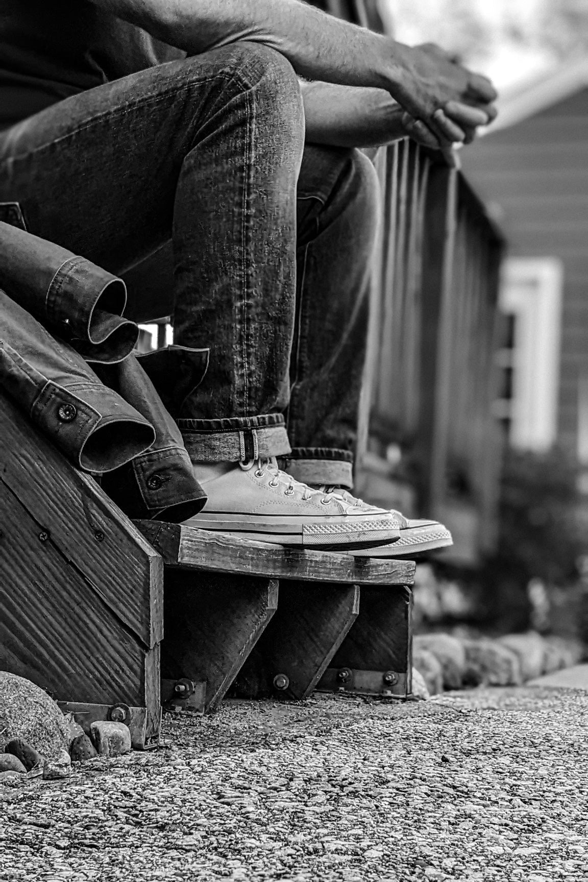 Real denim jeans with a worn texture and cuffed hems, worn by a man sitting on wooden steps paired with classic sneakers.