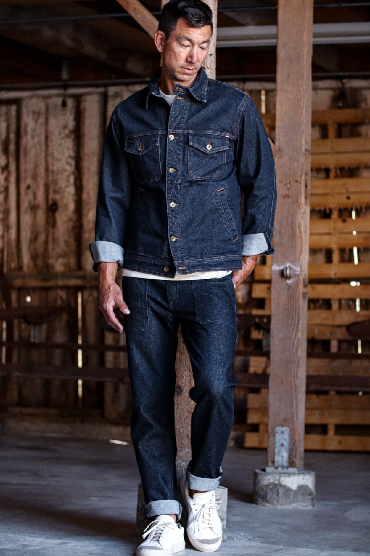 Denim jacket made in USA paired with matching jeans and white sneakers in a rustic indoor setting.