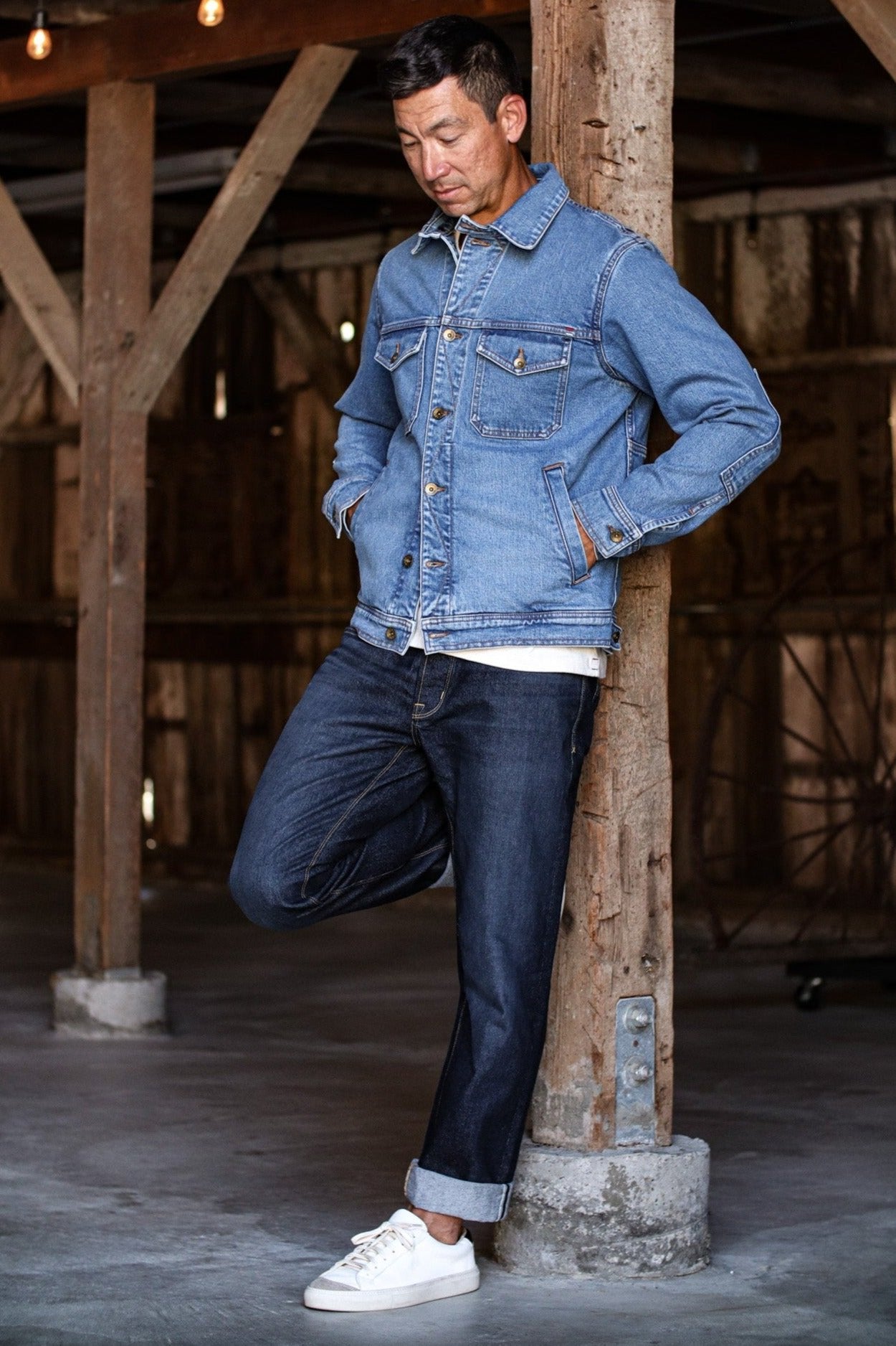 American made jean jacket styled casually with dark jeans and white sneakers in a rustic barn setting.