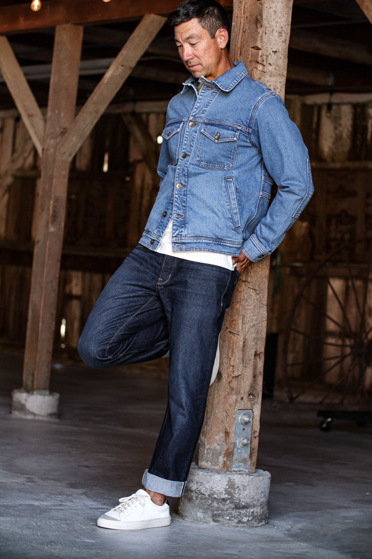 USA made canvas jacket paired with dark denim jeans and white sneakers in a rustic wooden barn setting.
