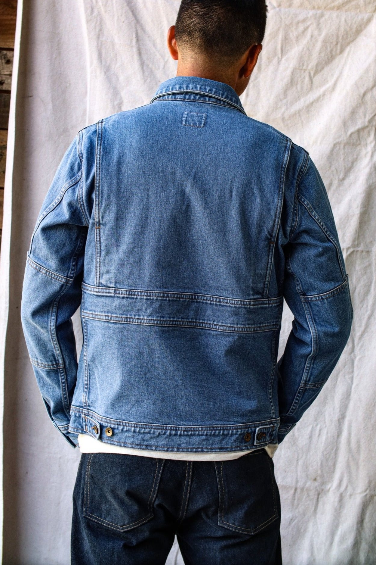 Back view of a light-wash denim jacket made in USA, featuring reinforced seams and adjustable waist tabs.
