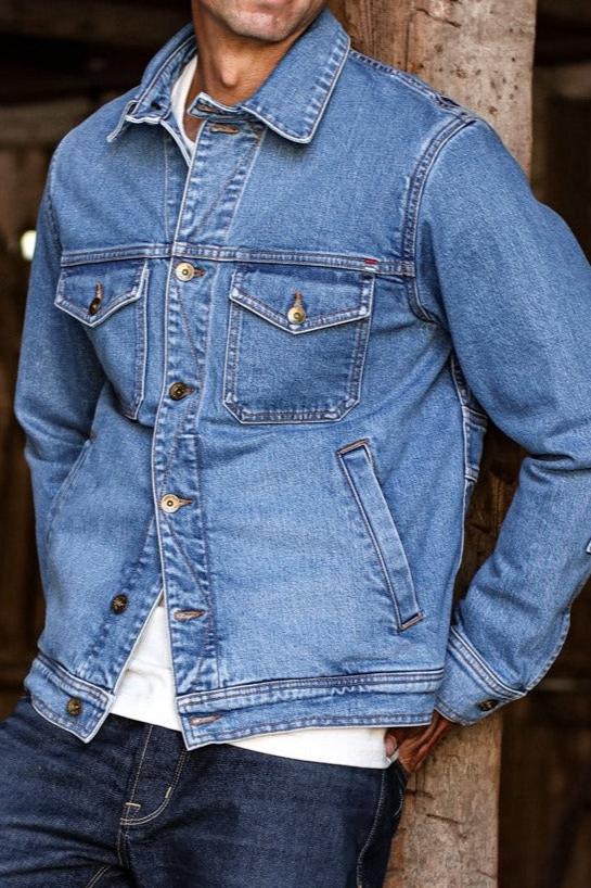 Jean jacket made in USA styled with casual denim and a white shirt, leaning against a rustic wooden post.