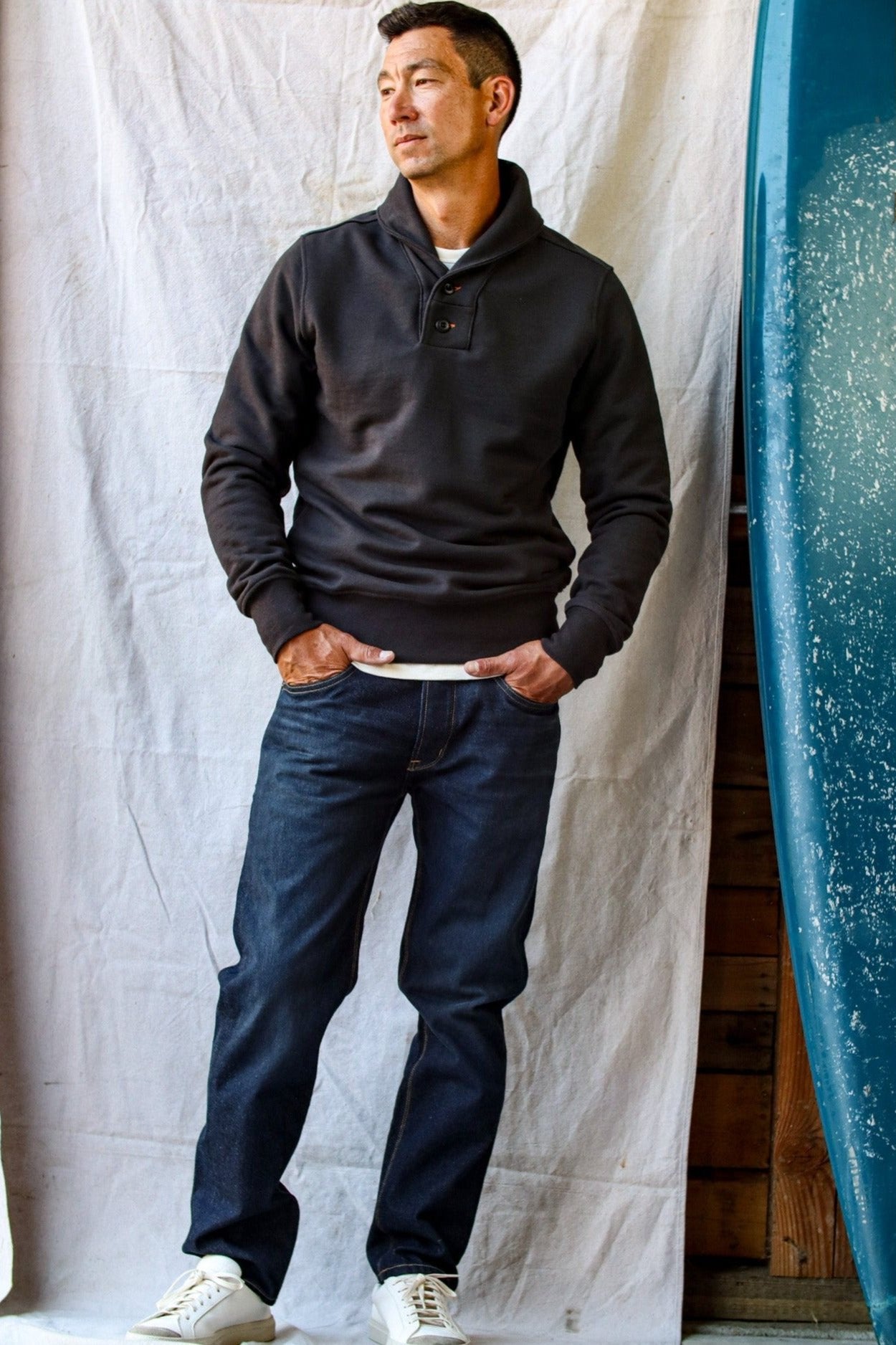 Men's shawl cardigan in black, styled casually with dark jeans and white sneakers against a coastal-inspired backdrop.