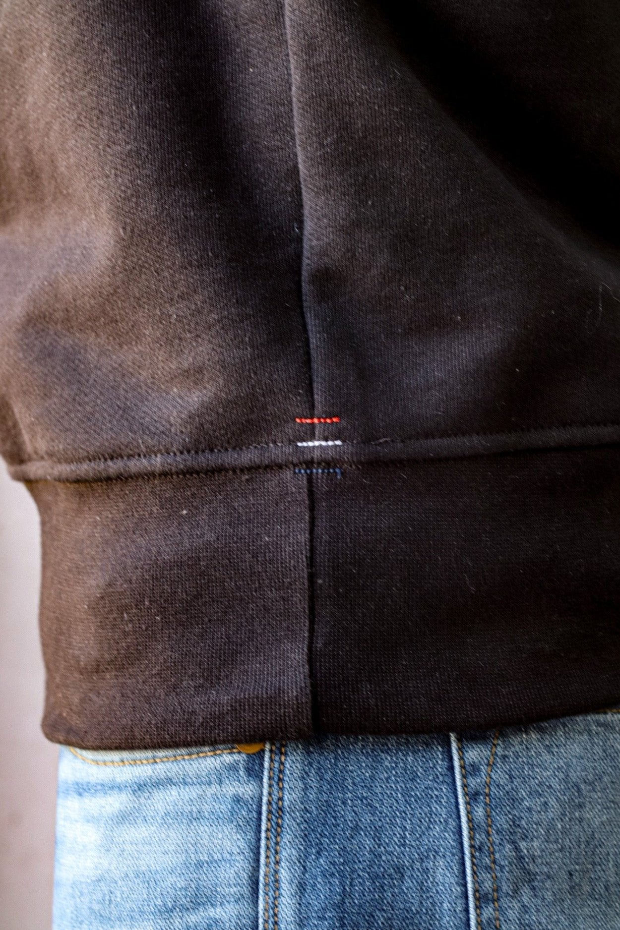 Collared cardigan men's hem detail in black, featuring fine stitching and subtle accents, paired with light-wash denim.