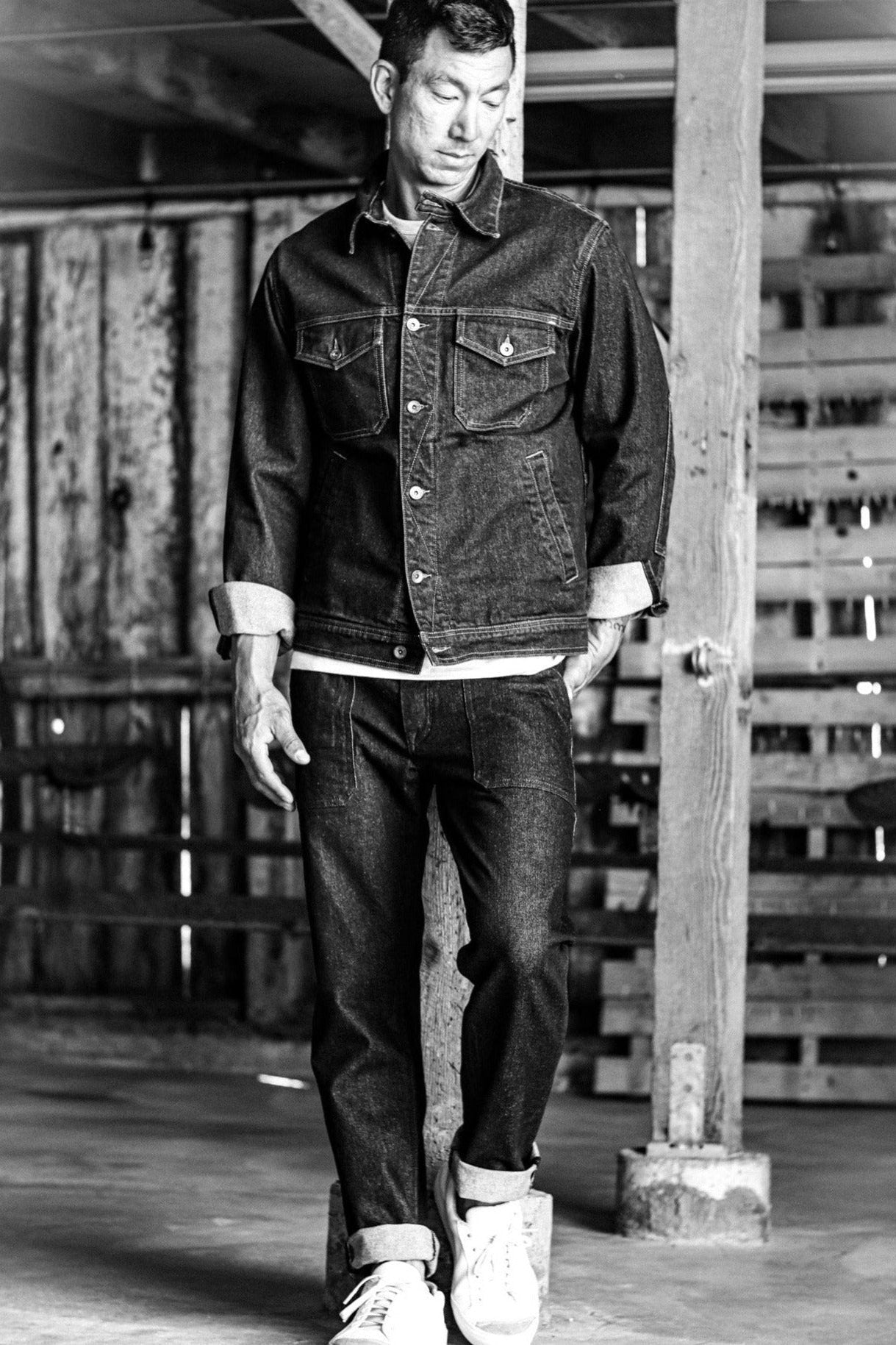 USA made denim jacket and jeans styled with rolled cuffs and white sneakers in a rustic barn setting.