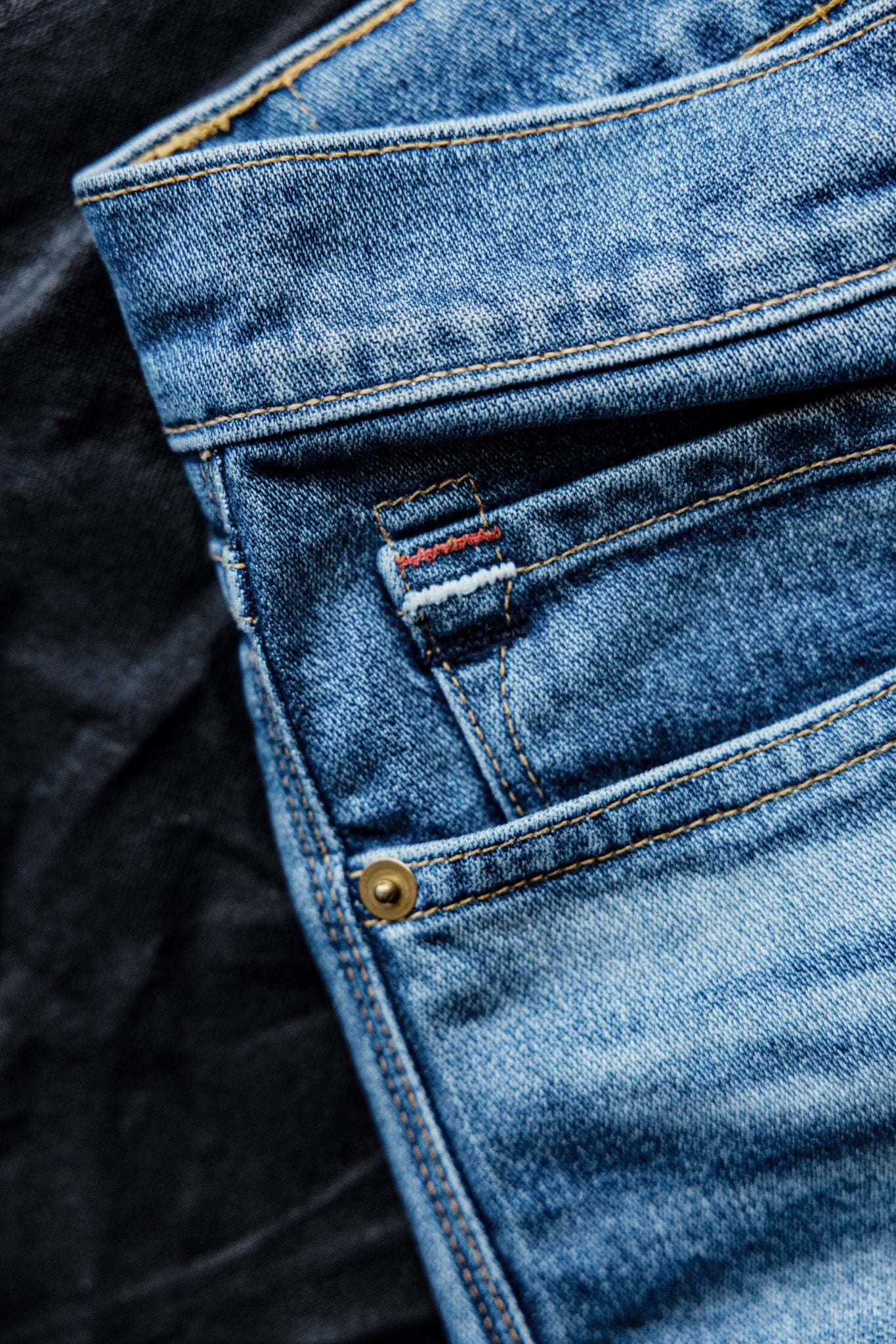 Mid-rise jeans for women with detailed stitching and a small embroidered loop, displayed on a dark fabric background.