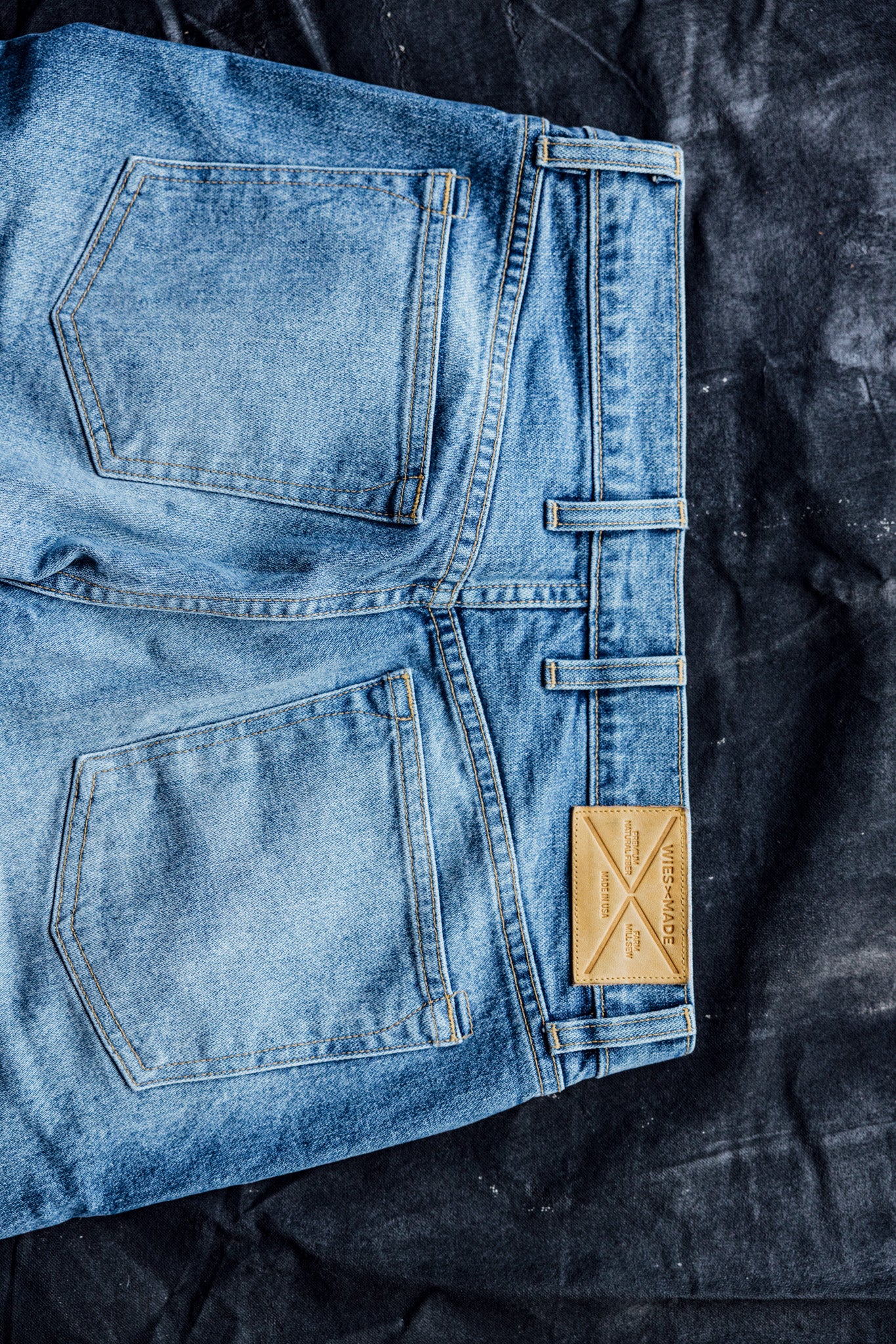 Denim pants for women featuring back pockets and a tan leather patch, displayed on a dark textured background.