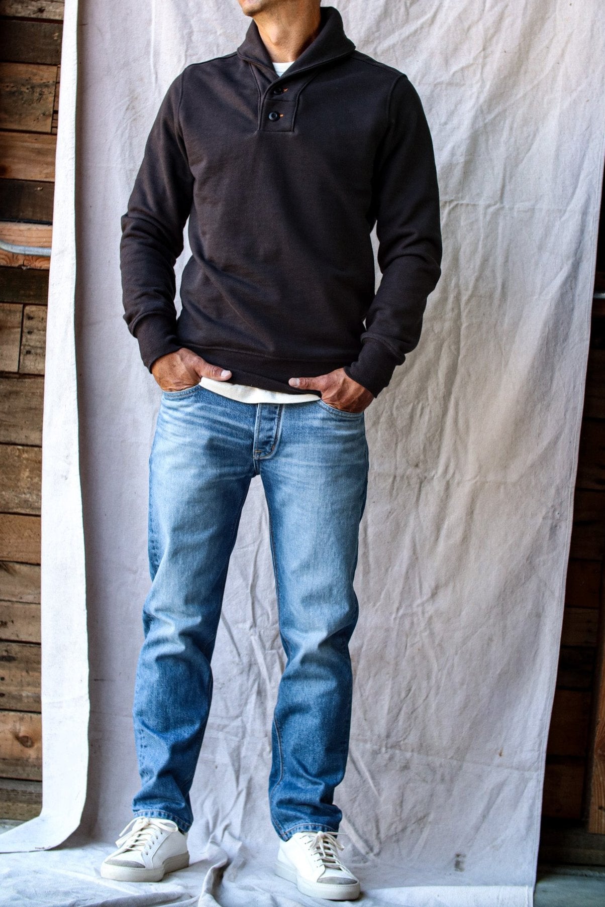 Men's raw denim jeans in a light wash with natural fading, styled with a black pullover and white sneakers against a neutral backdrop.