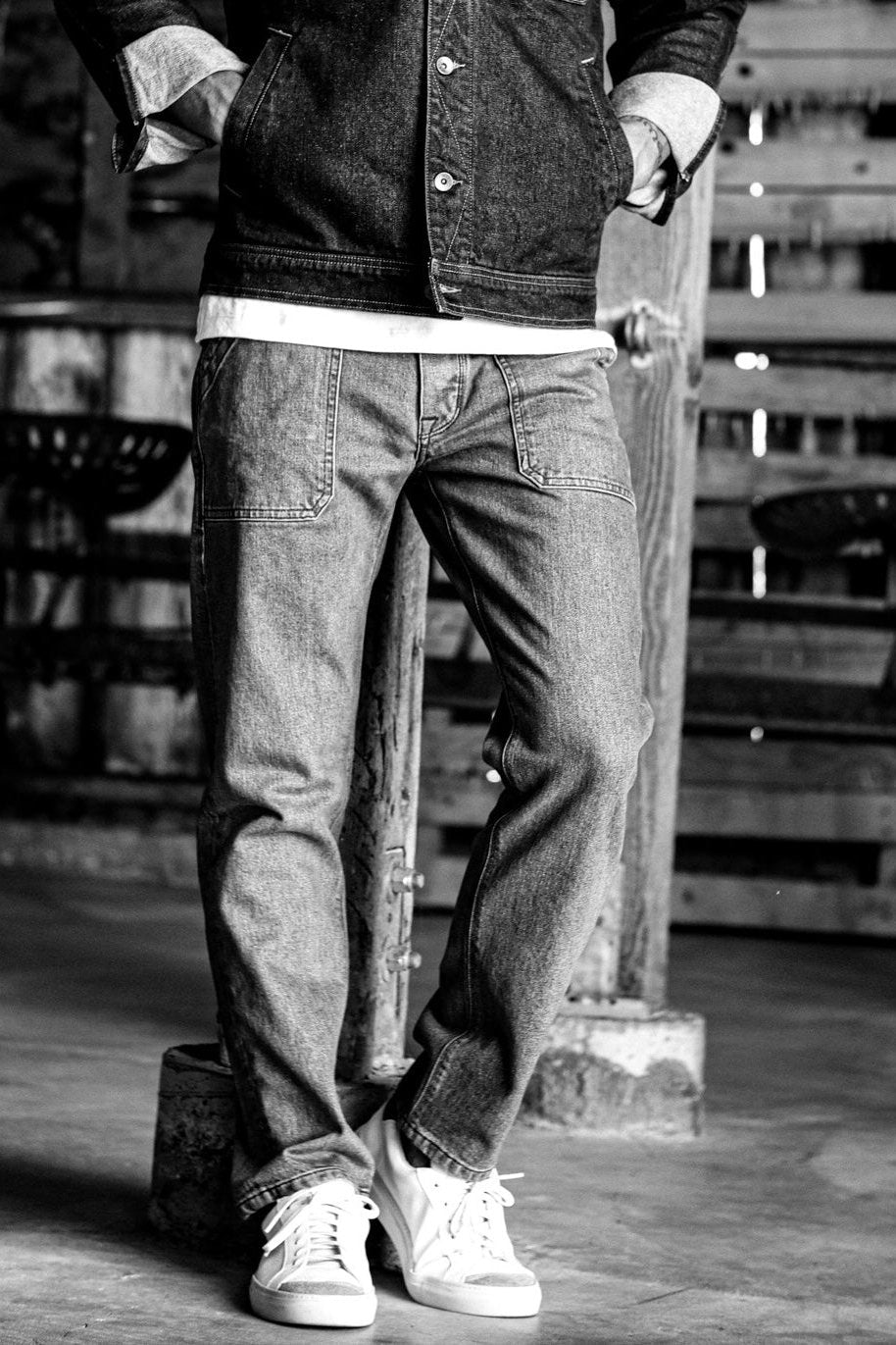 Selvedge denim jeans with large front pockets and a relaxed fit, styled with a denim jacket and white sneakers.