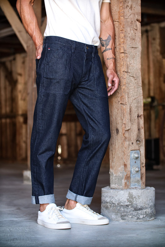 American denim jeans with a relaxed fit, cuffed at the ankles, worn by a man paired with white sneakers and a t-shirt.