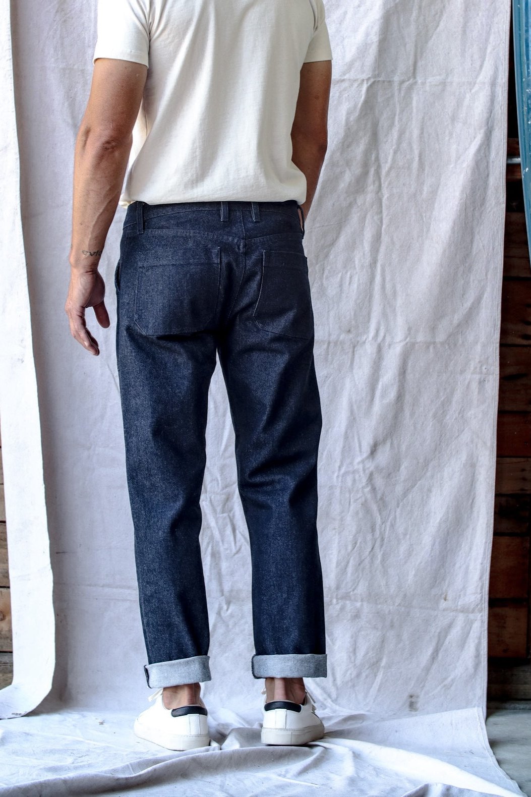 Real denim jeans with a relaxed fit and cuffed hems, worn by a man paired with a white t-shirt and sneakers, shown from the back.