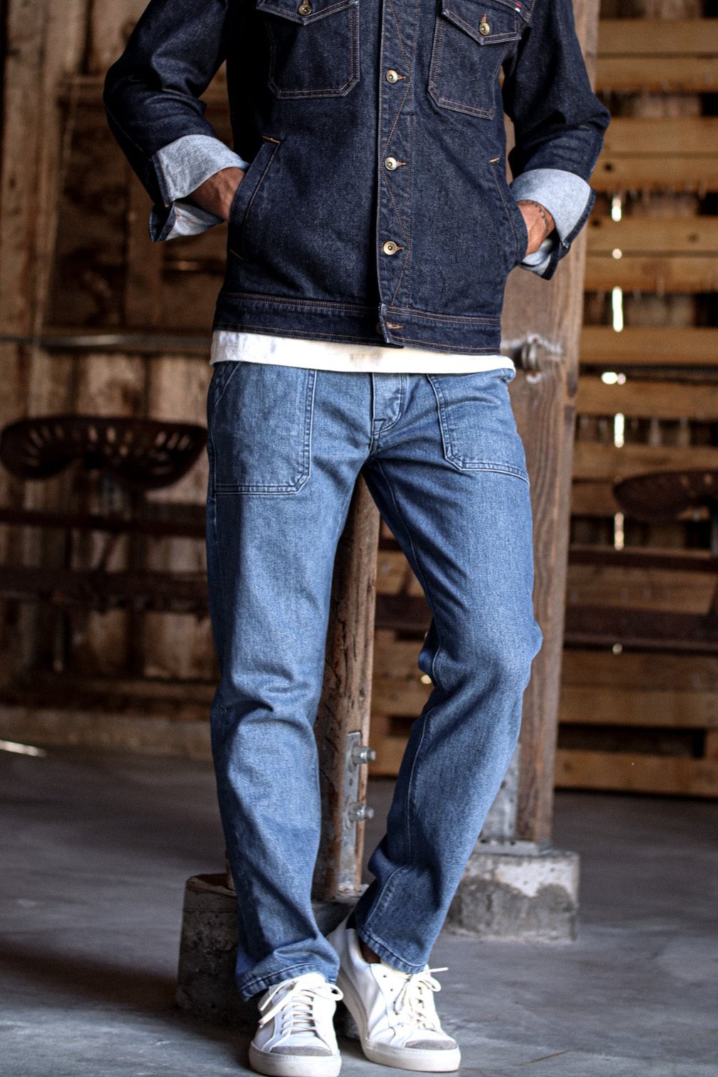 Raw denim jacket paired with light-wash raw denim jeans, styled with a white shirt and sneakers in a rustic setting.