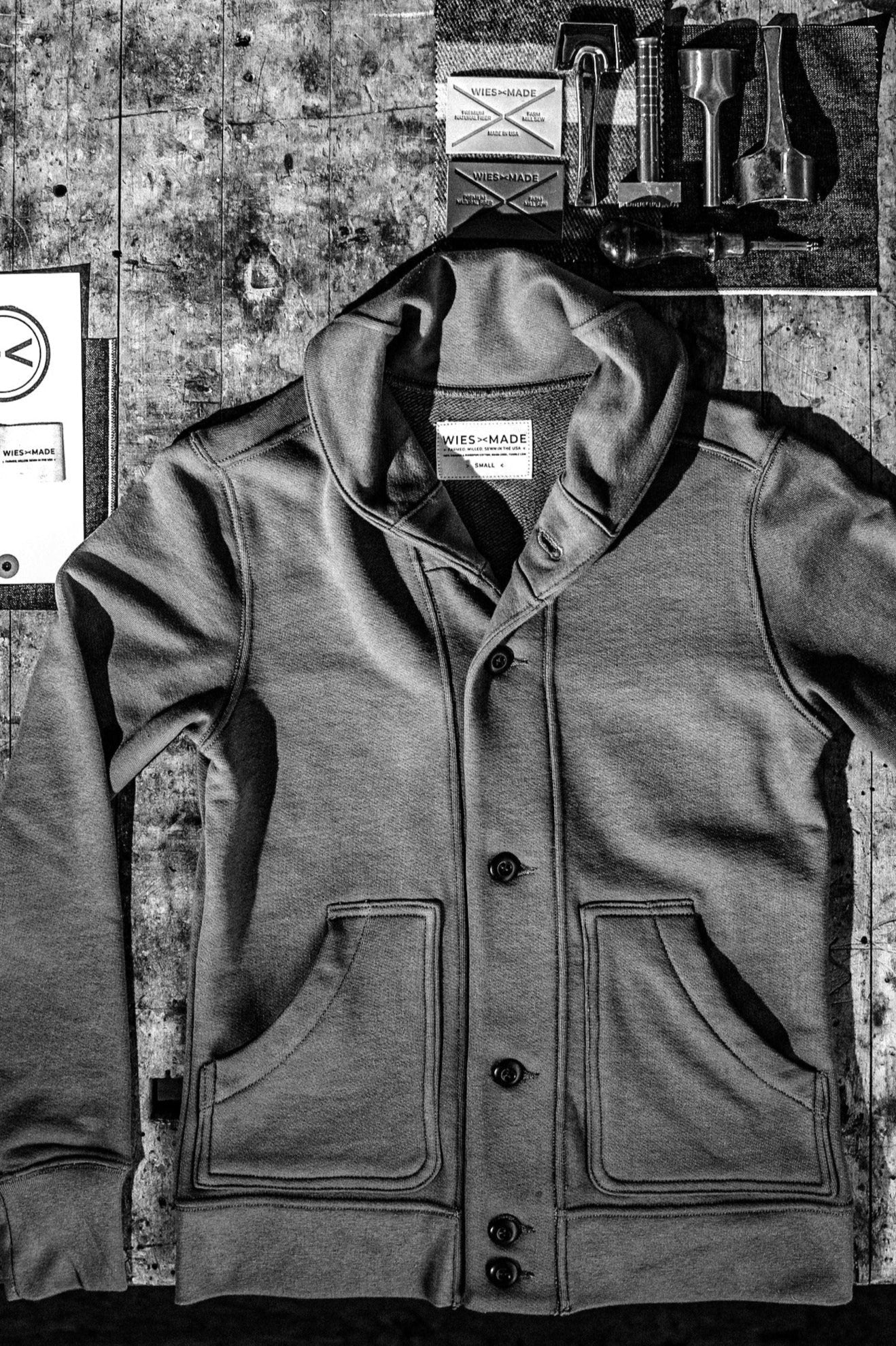 Shawl cardigan men's style laid flat, showcasing front pockets and a detailed collar design on a rustic surface.