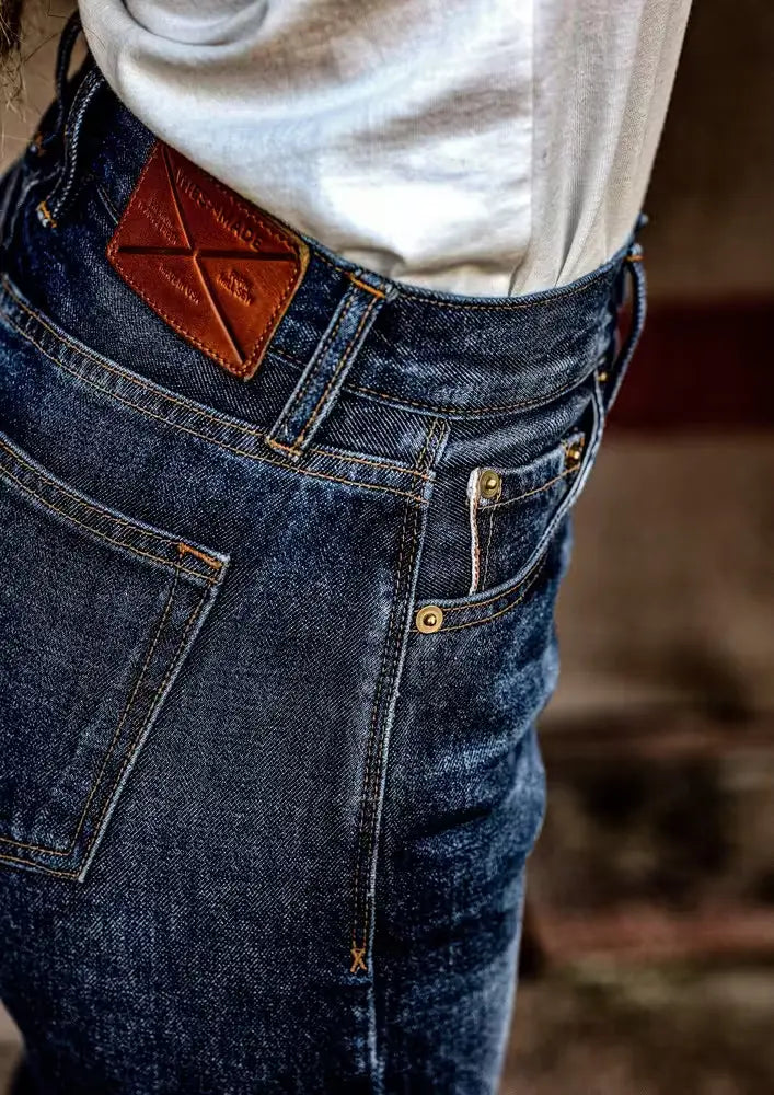 Close-up of Sidney Fit Jean in Ocean Washed Selvedge Denim, featuring a high-rise straight leg fit, detailed stitching, & a leather brand patch, paired with a tucked-in white shirt