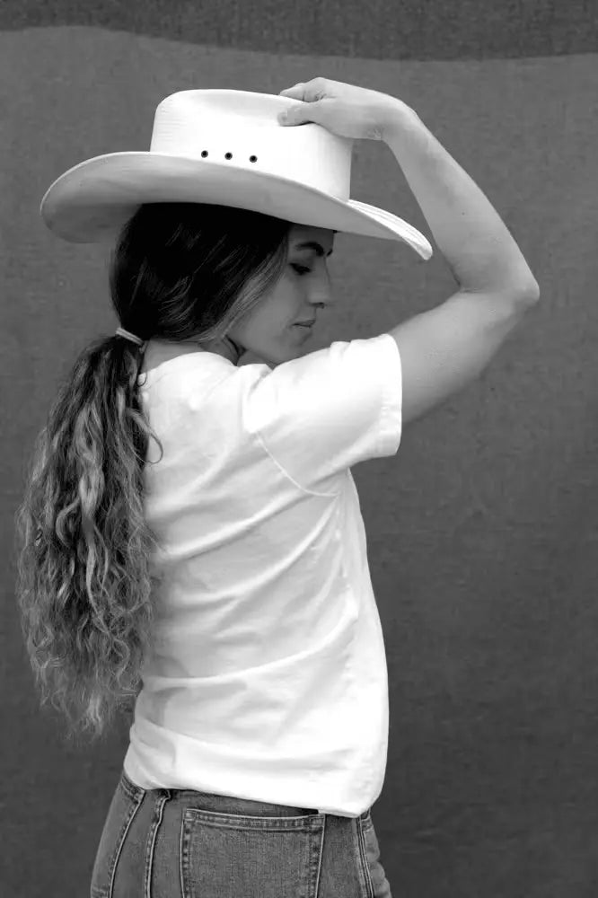 Bolinas Heavyweight Tee in 8oz 100% cotton, natural color, worn by a woman with long, wavy hair, styled with a white cowboy hat and light denim jeans, standing against a neutral textured background