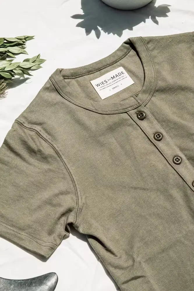Reyes Henley in olive color for women, made from heavyweight 8oz 100% cotton, featuring a three-button placket, laid flat on a white surface with greenery in the background