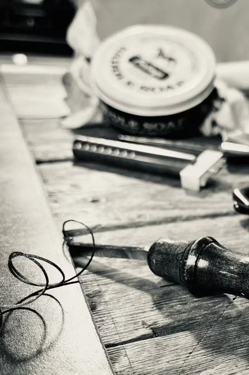 Leatherworking tools and black thread on a wooden surface, showcasing craftsmanship for creating an 8oz Latigo Belt