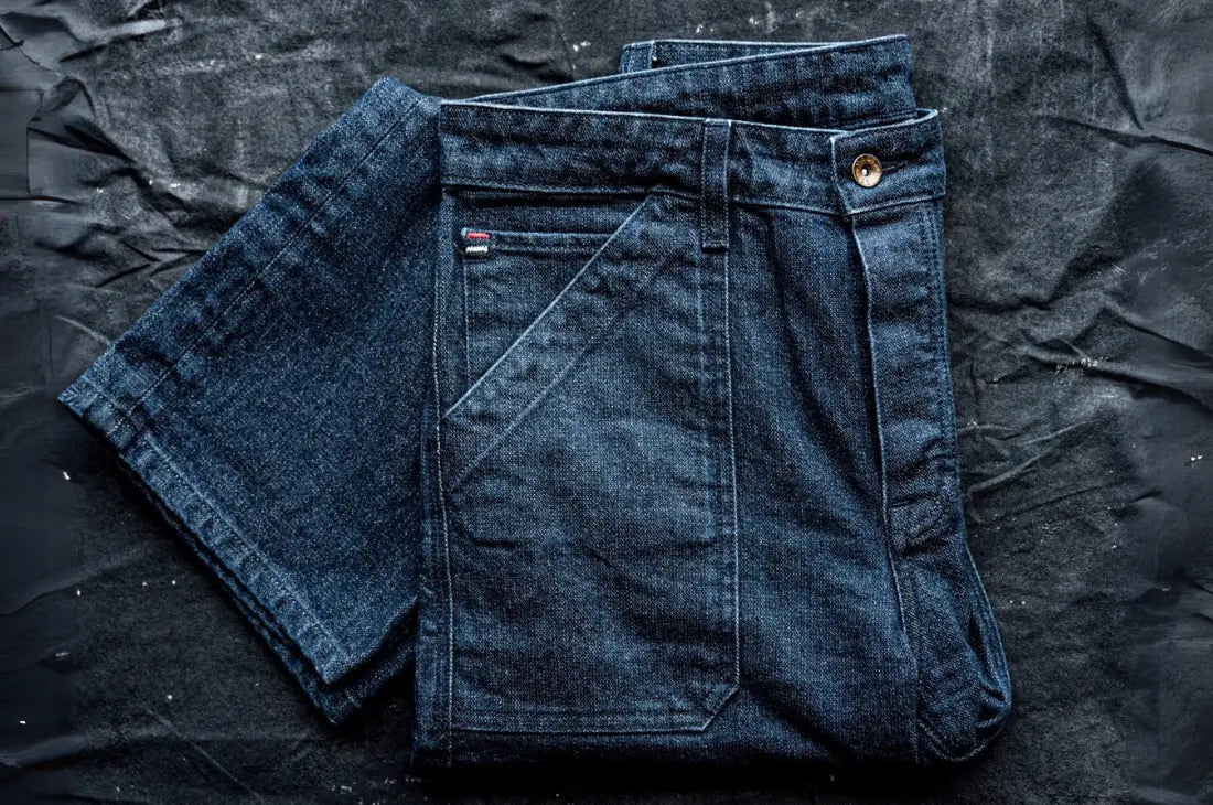 14 oz denim jeans in deep indigo, neatly folded on a textured black surface, showcasing durable fabric and reinforced stitching