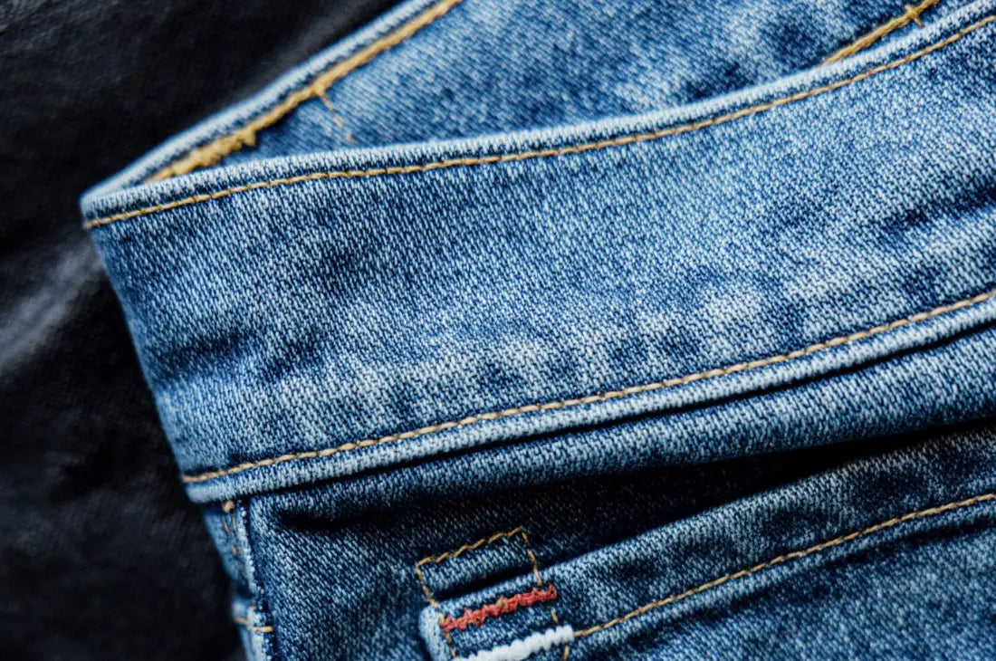Premium denim jeans folded to highlight stitching details, textured fabric, and a selvedge edge