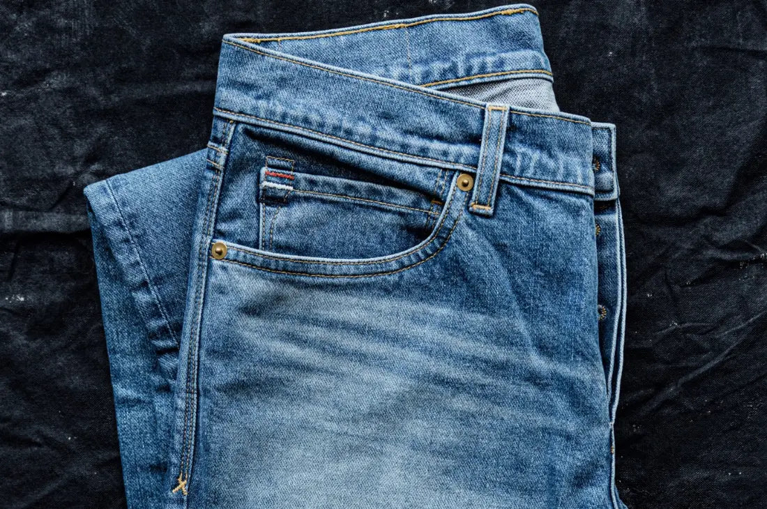 Ring-spun cotton jeans folded neatly, featuring a faded wash and durable stitching against a dark fabric background