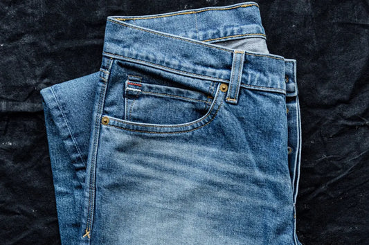 Ring-spun cotton jeans folded neatly, featuring a faded wash and durable stitching against a dark fabric background