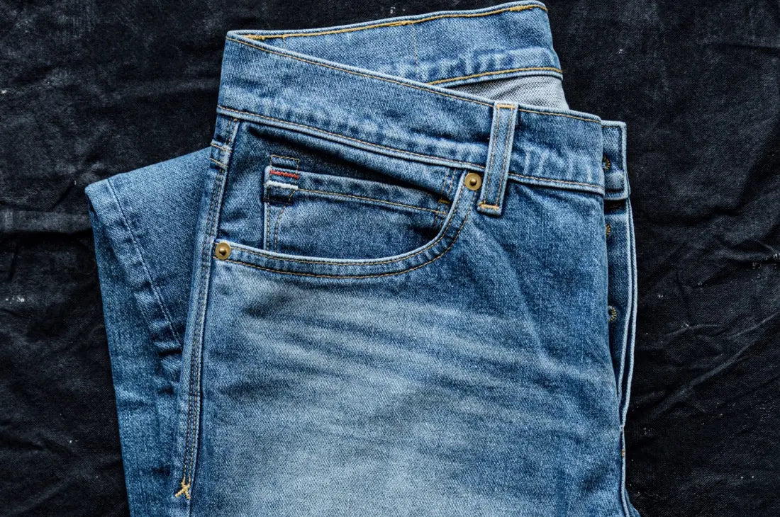 Small-batch clothing jeans folded to showcase faded denim, precise stitching, and premium fabric texture