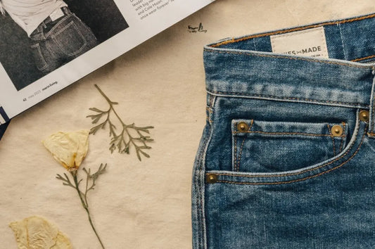 High-quality denim jeans with brass rivets, styled alongside dried flowers and an open magazine