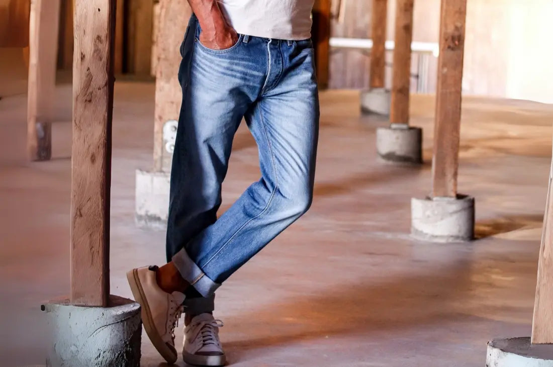 Denim jeans for men styled casually with a white t-shirt and sneakers in a rustic setting