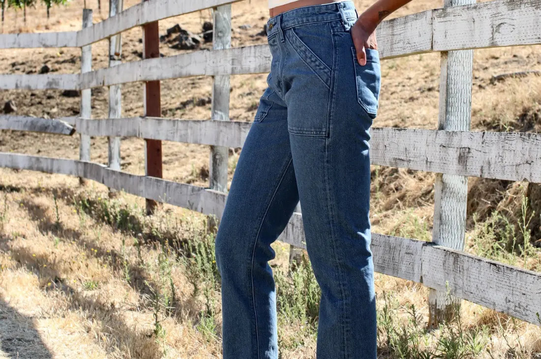 Heavyweight denim jeans in medium blue worn outdoors near a rustic wooden fence.