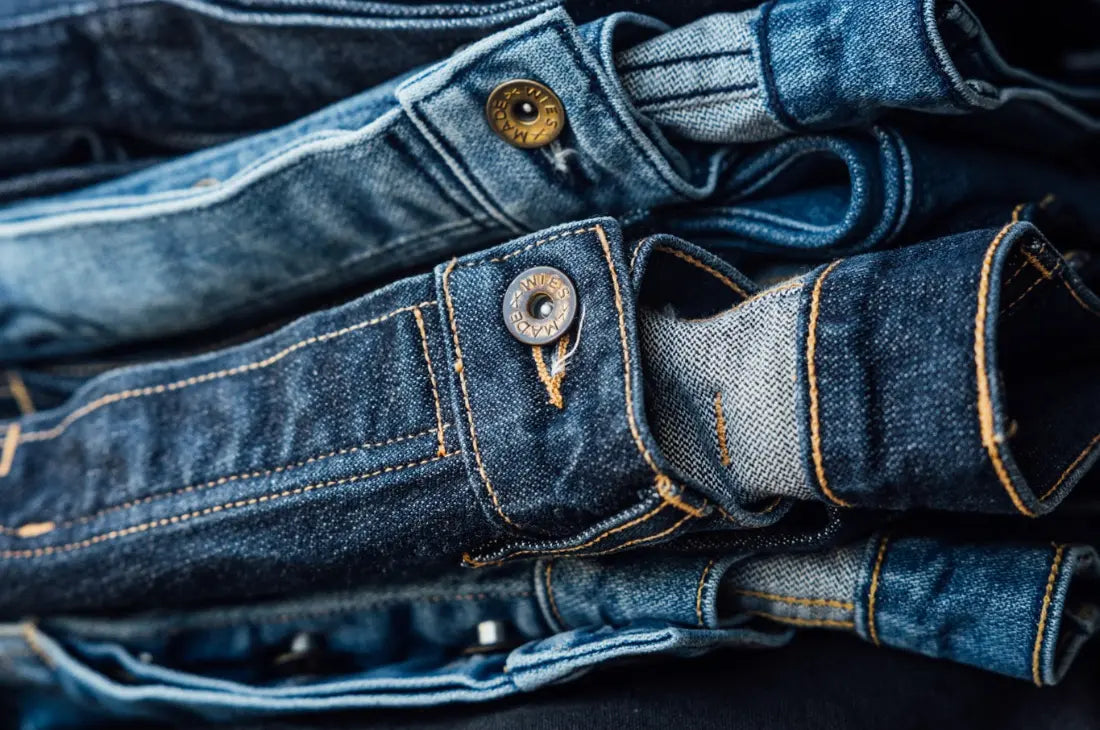Men's denim jeans stacked in a pile, showcasing different shades of blue with visible stitching and metal buttons