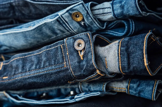 Men's denim jeans stacked in a pile, showcasing different shades of blue with visible stitching and metal buttons
