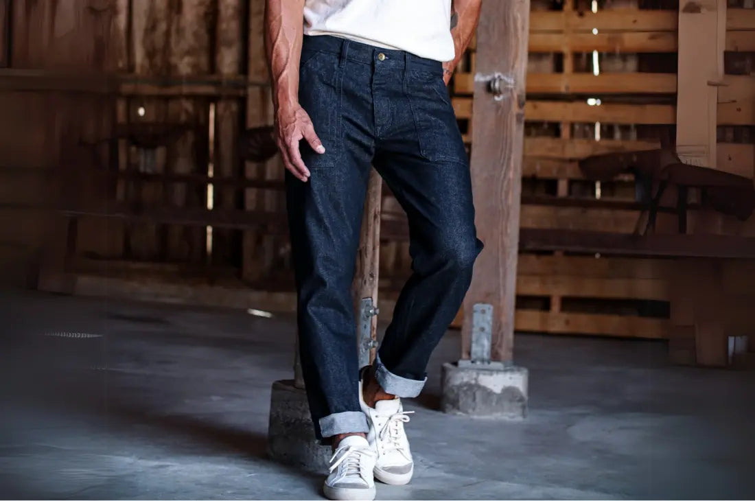 Premium denim jeans in a dark wash, cuffed at the ankles and paired with white sneakers in a rustic setting