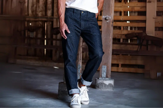 Premium denim jeans in a dark wash, cuffed at the ankles and paired with white sneakers in a rustic setting