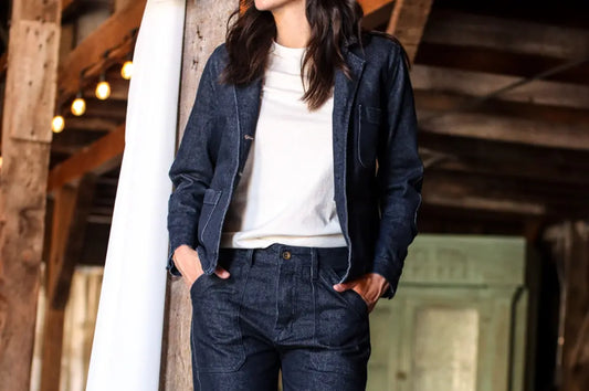 Vintage jeans for women paired with a dark denim jacket and white shirt in a rustic barn setting.
