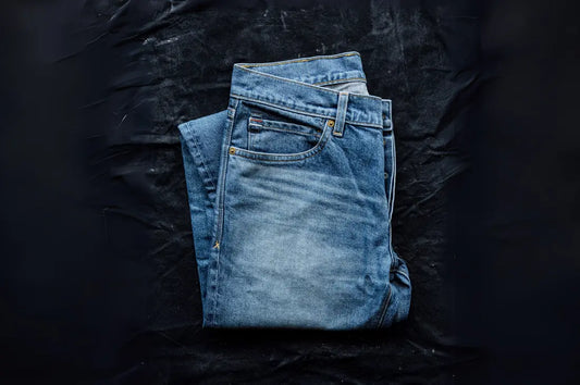 Washed denim pants neatly folded on a dark textured background, featuring a faded look, durable stitching, and classic design