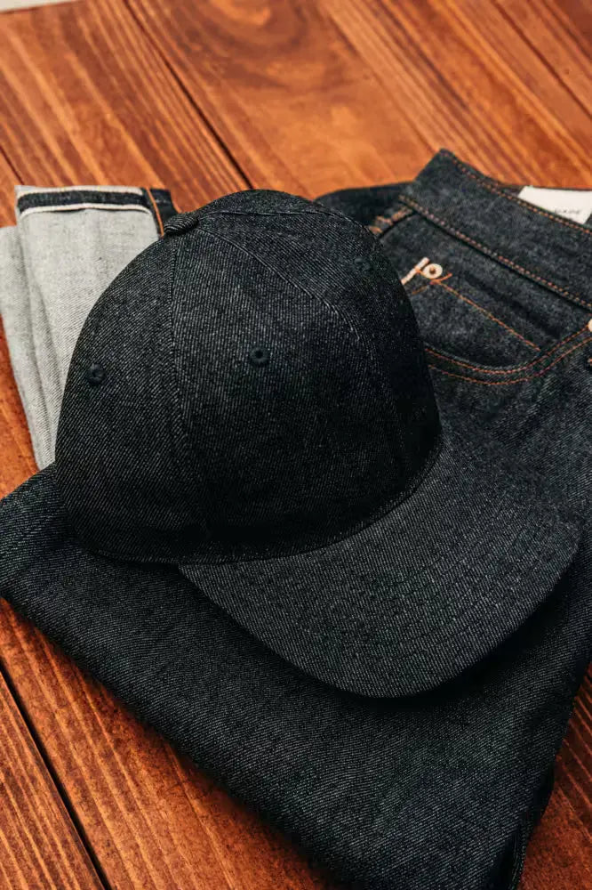 Selvedge denim ballcap in raw color displayed on folded matching jeans on a wooden surface