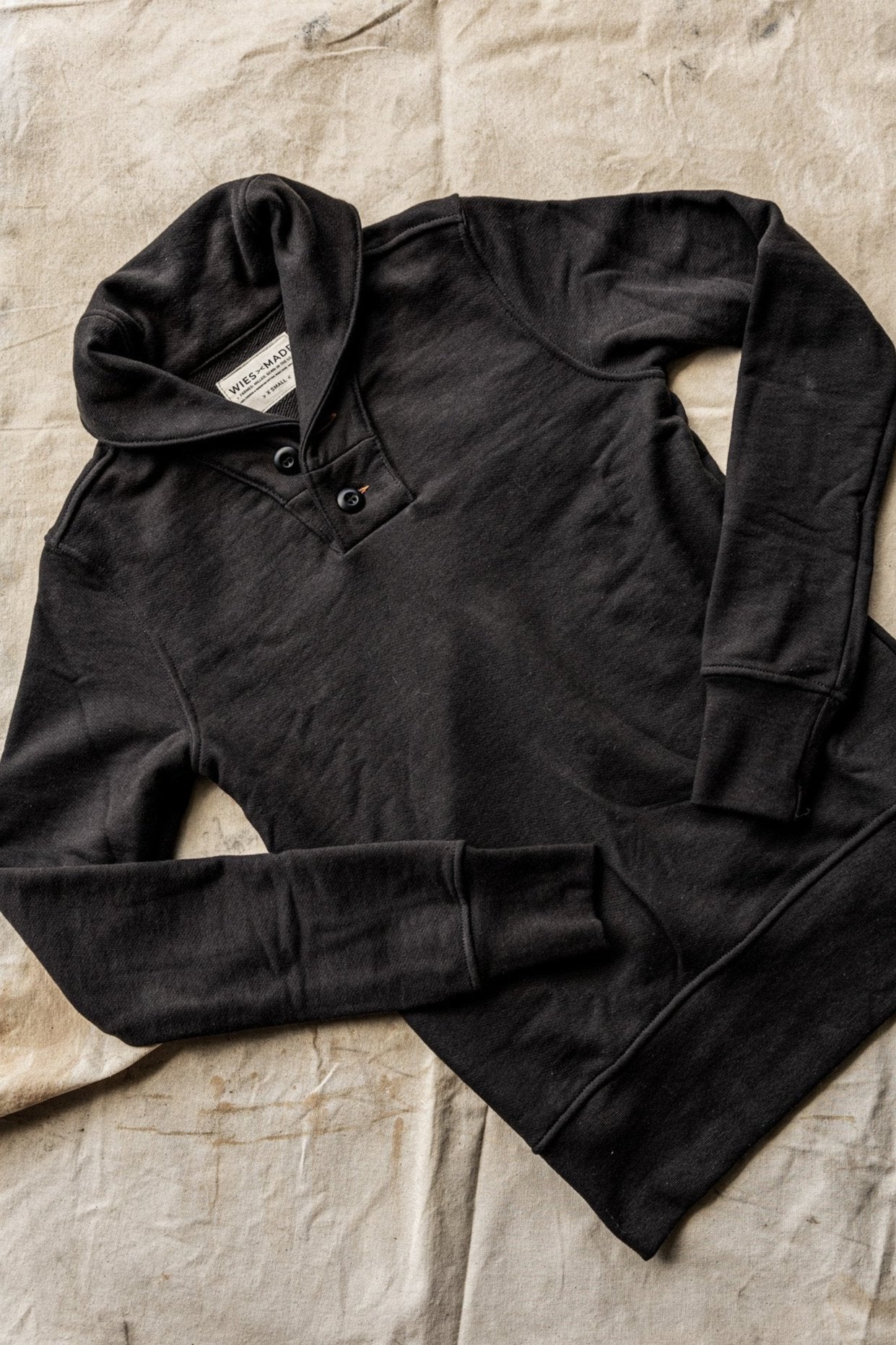 Collared cardigan men's design in black, laid flat to showcase its button details and cozy fabric texture.