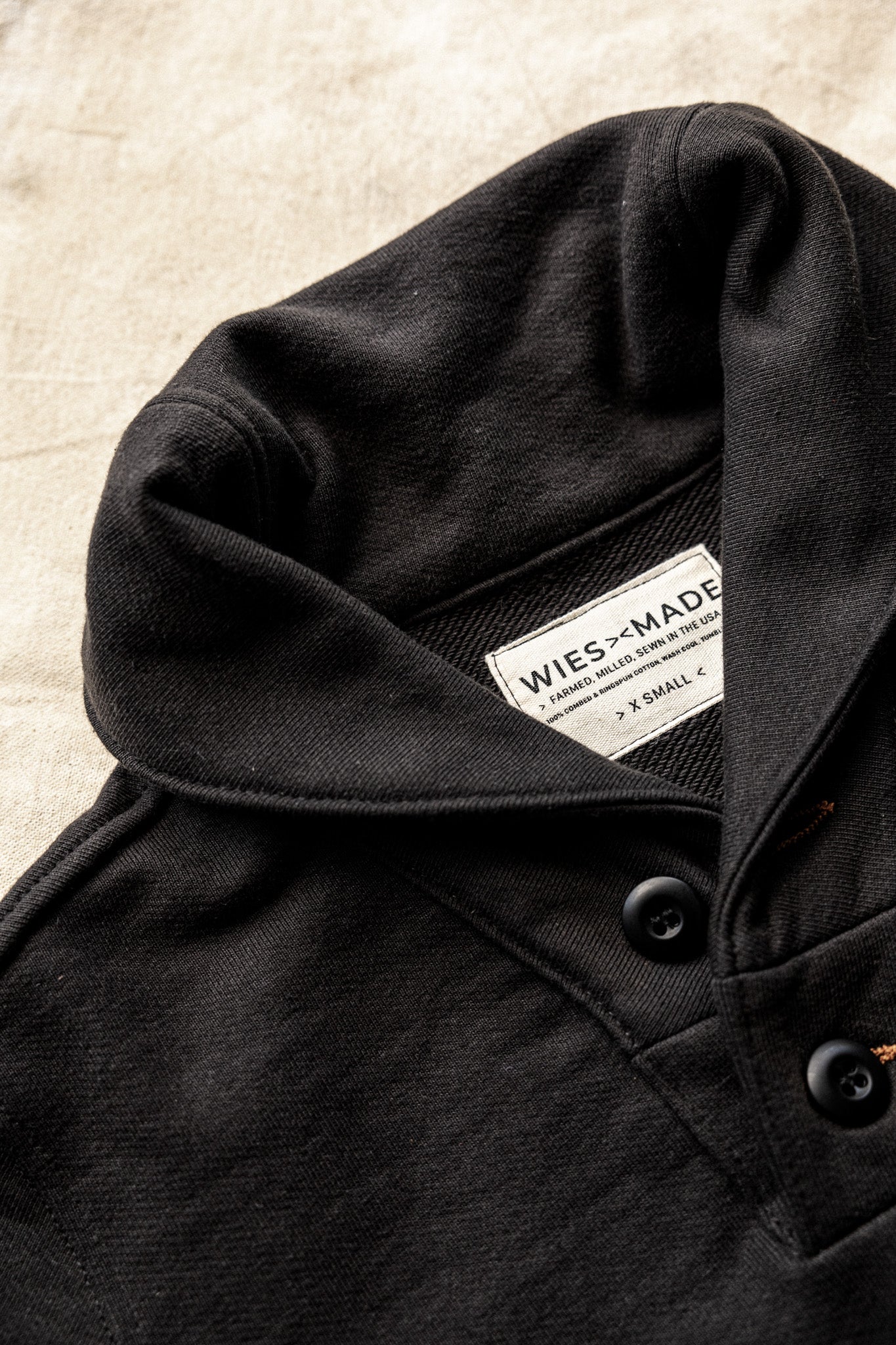Shawl cardigan men's collar detail in black, featuring button accents and a branded label on soft fabric.