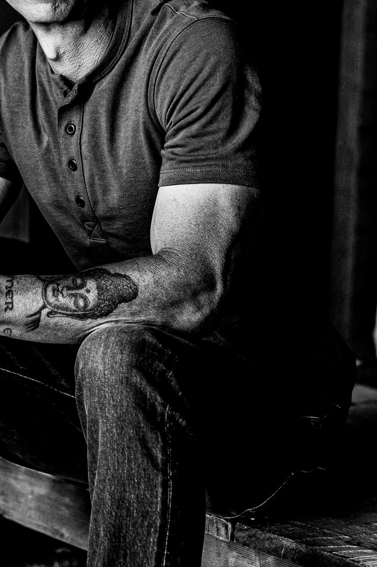 Seated man in a short-sleeve four-button Bolinas Henley and dark jeans, shown in black and white.