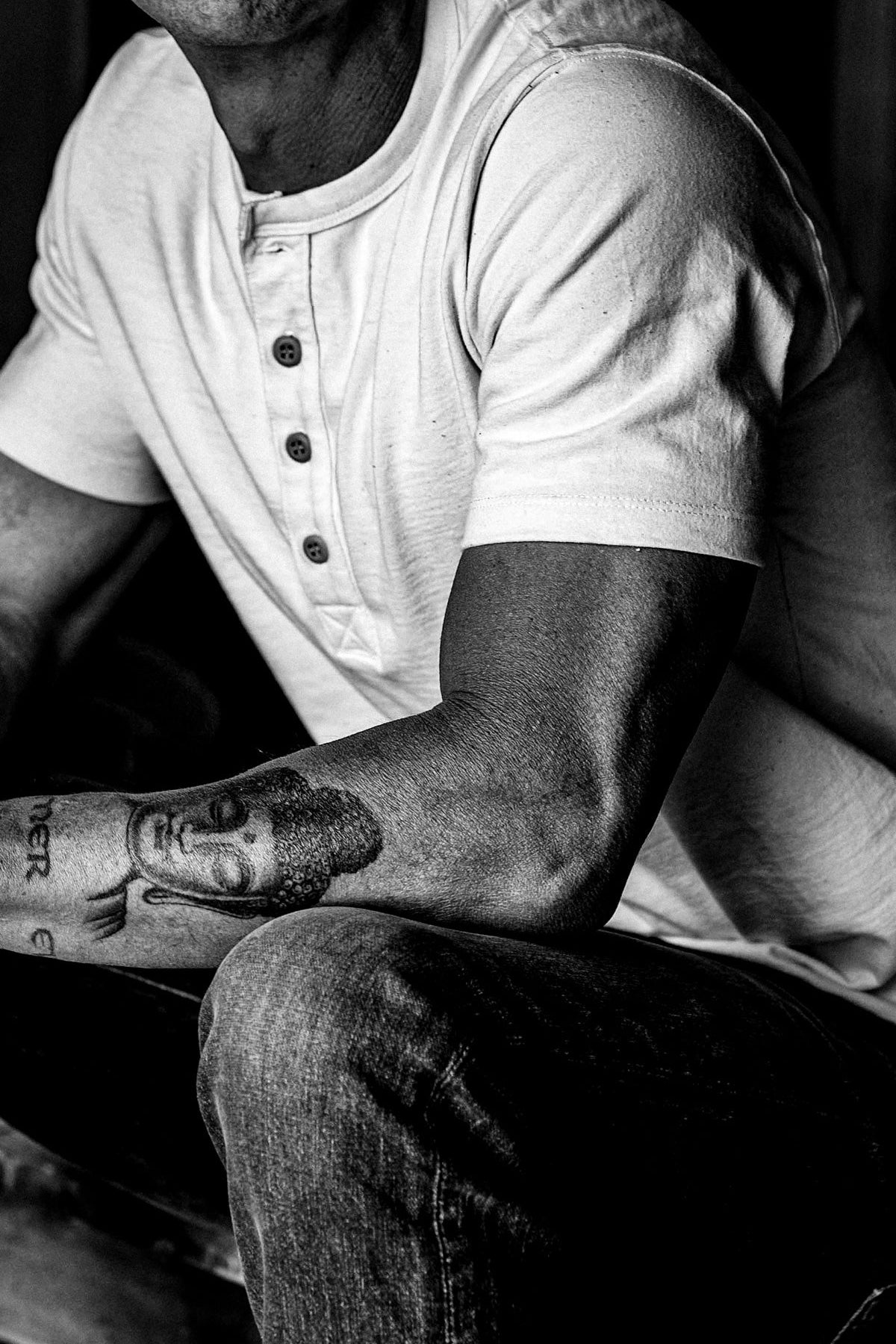 Seated man wearing a natural four-button Bolinas henley with dark denim jeans, shown in black and white.