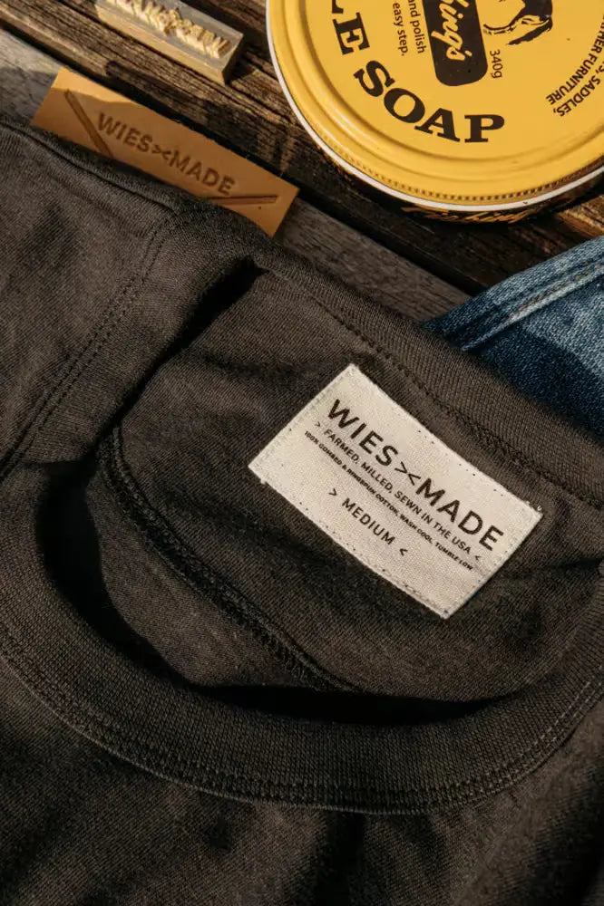 Men's Bolinas Tee in basalt color with Wiesz-Made branding displayed alongside denim & saddle soap on a wooden surface