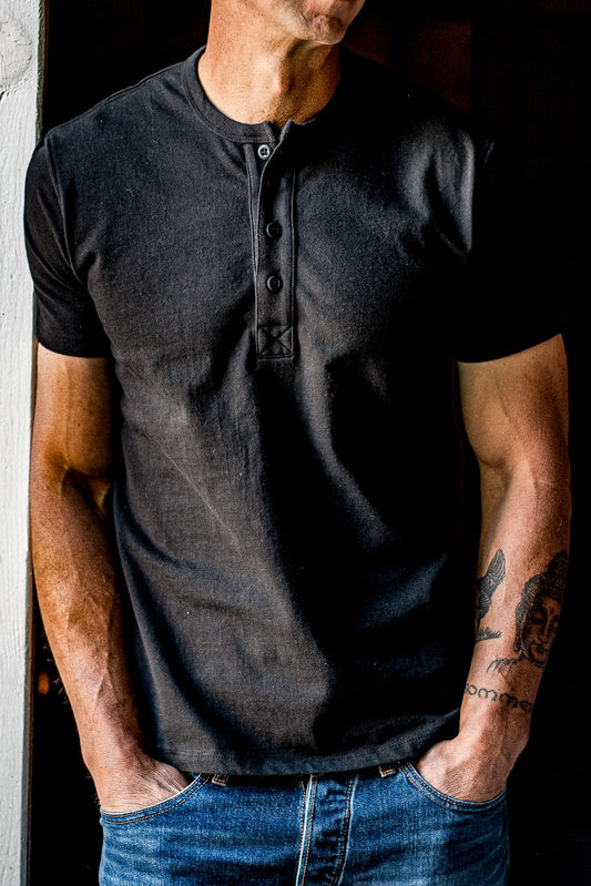 Man wearing a dark basalt four-button short-sleeve Bolinas Henley with blue jeans.