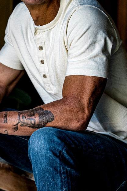 Man seated in natural four-button Bolinas Henley paired with blue denim jeans.