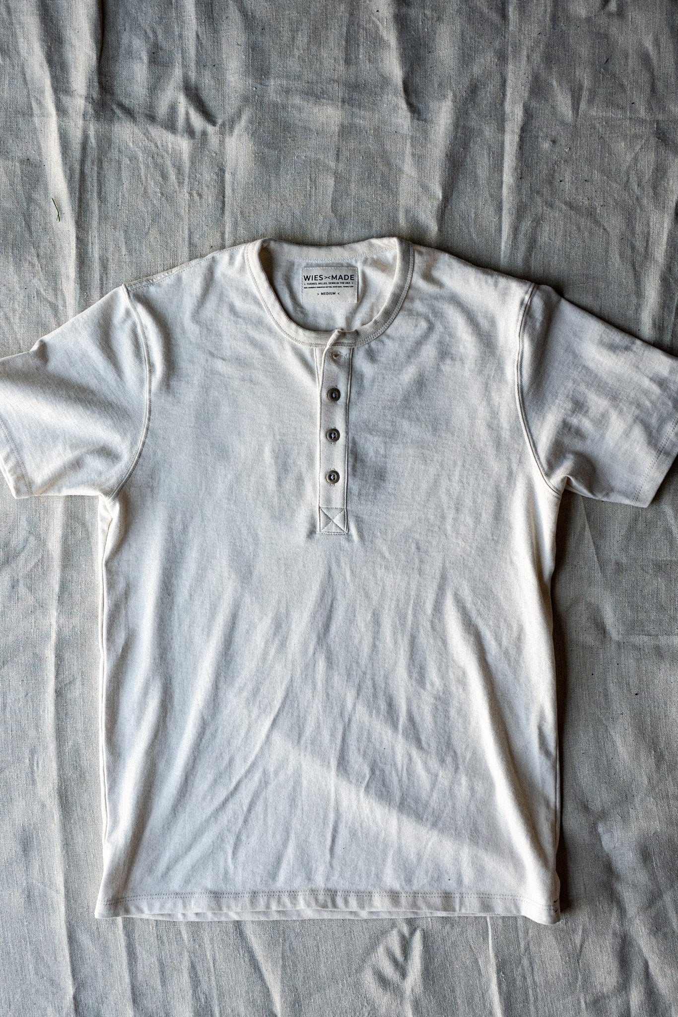 Natural cream four-button short-sleeve heavyweight cotton Henley laid flat on linen backdrop.