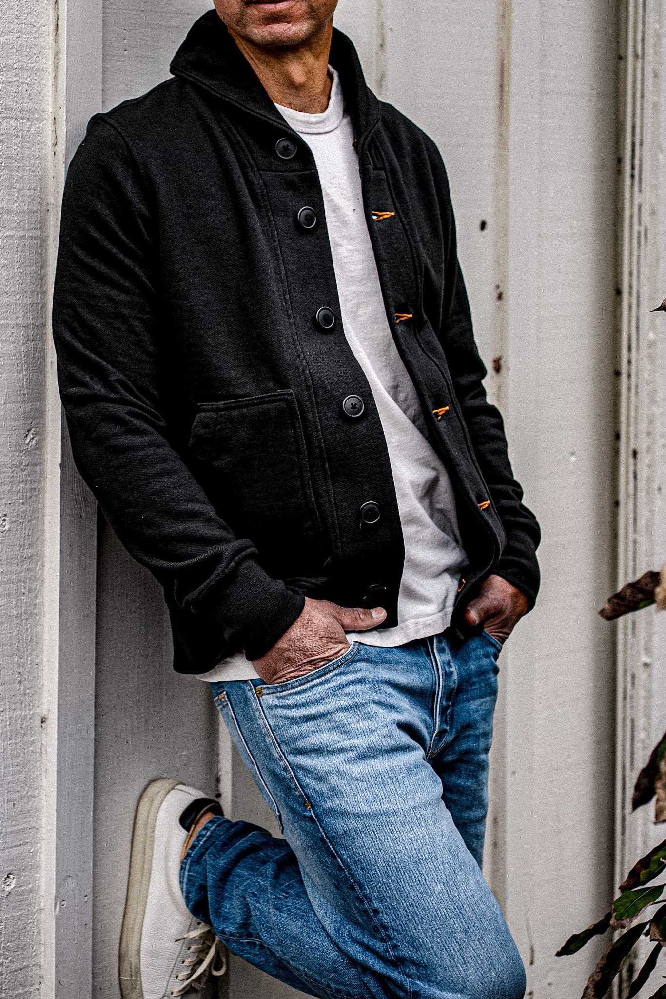 Man in basalt black French terry shawl cardigan with orange keyhole stitching, worn over a white tee with light wash jeans.